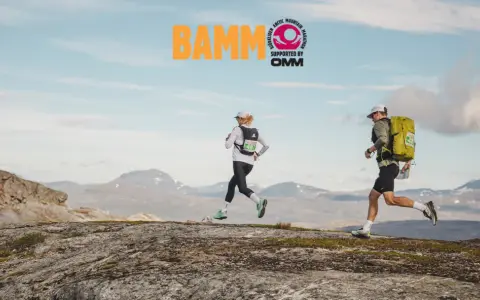Två löpare springer över kargt fjällandskap. BAMM-loggan syns högt upp.