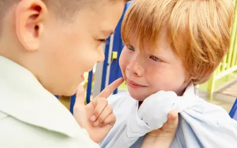 Ein Junge zeigt mit dem Finger auf das Gesicht eines anderen Jungen, der verängstigt wirkt. Ein Beispiel für Mobbing in der Schule.