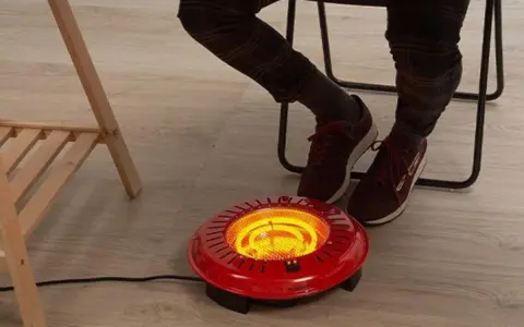 Persona calentando sus pies con un brasero eléctrico rojo bajo un escritorio.