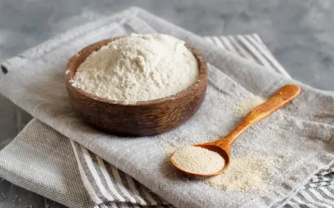 Mąka gryczana w drewnianej misce i na łyżce. Czy mąka gryczana ma gluten? Nie, jest bezglutenowa.