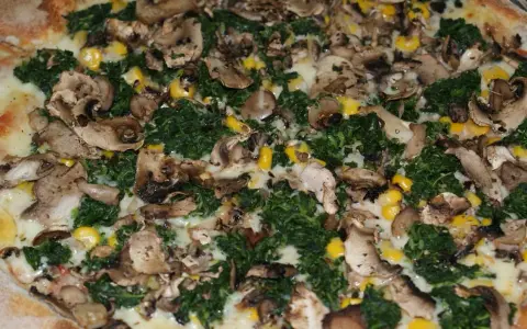 Pyszna pizza ze szpinakiem, grzybami i kukurydzą, obficie posypana serem.