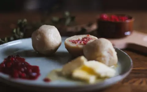 En tallrik med pitepalt, lingonsylt och smör. En halv palt visar en fyllning av fläsk. Perfekt för ett recept på pitepalt.