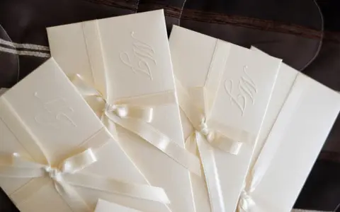 Eleganckie zaproszenia ślubne z monogramem, ozdobione satynową wstążką. Idealne, by dowiedzieć się, jak zrobić zaproszenie w Wordzie.