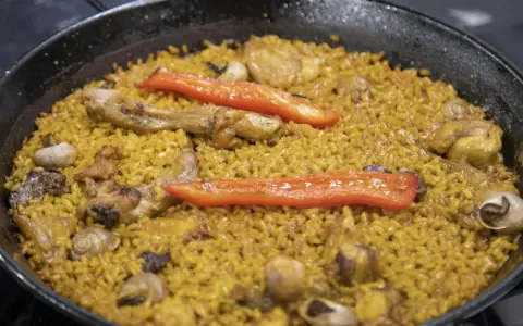 Paella de arroz con carne, pimientos rojos y caracoles. Un plato tradicional español lleno de sabor.