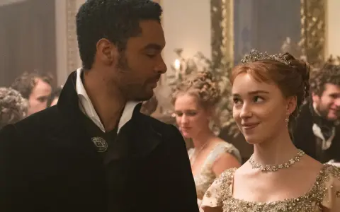 En ung kvinna med tiara och en man i elegant klädsel möts med blickar. Kanske en scen från rollistan i familjen Bridgerton.