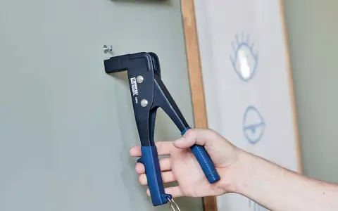 Herramienta para colgar en pladur. Un tornillo se fija a la pared con una remachadora.
