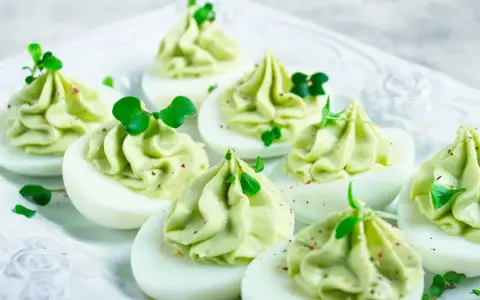 Uova ripiene pasquali, guarnite con crema verde e germogli freschi, pronte per essere gustate.