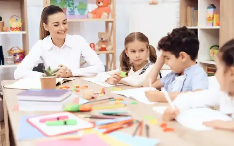 Uśmiechnięta nauczycielka przedszkola z dziećmi przy stoliku, tworząc inspirujący list motywacyjny dla przyszłych pedagogów.