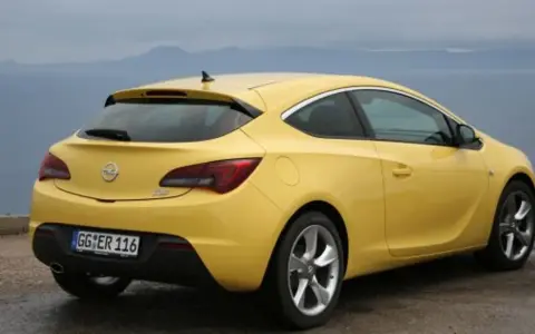 Żółta Astra GTC z tablicą rejestracyjną GG ER 116 stoi na tle morza i gór.