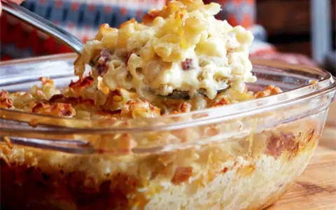 En sked lyfter upp en portion krämig, gammaldags makaronipudding ur en glasform.