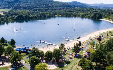 Sommerliche Idylle am Borkener See mit vielen Badegästen, Wasserrutsche und schattigen Plätzen unter Bäumen.