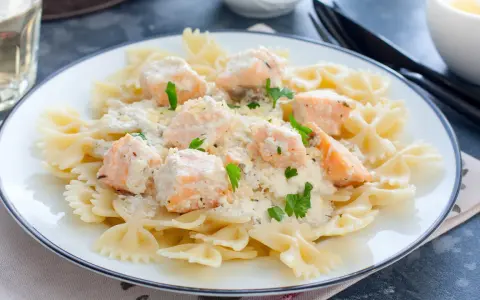 Pyszny makaron farfalle z kawałkami łososia w kremowym sosie, posypany natką pietruszki. Idealny na szybki obiad.