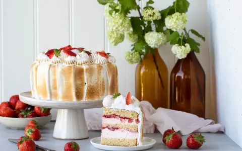 Eine köstliche Erdbeer Baiser Torte mit frischen Erdbeeren und zartem Baiser. Ein Stück der Torte zeigt die saftigen Schichten.