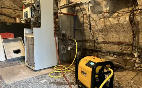 Un technicien effectue le desembouage d'une pompe à chaleur dans une chaufferie. L'équipement est relié à la chaudière par des tuyaux jaunes.