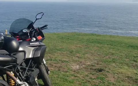 Motocykl Ducati zaparkowany na trawie z widokiem na morze. Marzenie o podróży przez Szwecję motocyklem.