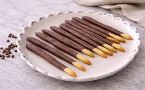 Assiette de mikado maison, bâtonnets de biscuit enrobés de chocolat, avec quelques grains de café à côté.