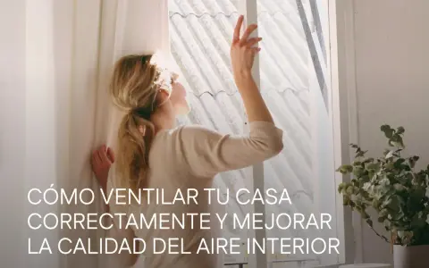 Mujer abriendo ventana para mejorar la **calidad del aire interior**. La luz del sol ilumina su cabello rubio recogido.