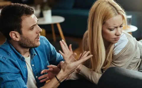 Hombre con expresión de enfado gesticula hacia su pareja, quien lo mira con desprecio, evidenciando una discusión.