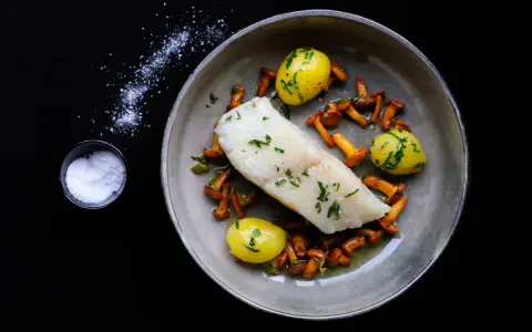 Ein köstliches Heilbutt-Rezept: zartes Fischfilet mit kleinen Kartoffeln und Pfifferlingen, garniert mit frischen Kräutern.