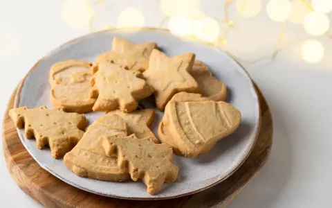 Assortiment de sablés de Noël en forme de sapins, étoiles et cloches, parfaits pour accompagner un chocolat chaud.