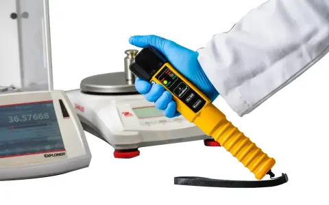 Ręka w rękawiczce trzyma alco sensor 4. Obok wagi laboratoryjne.