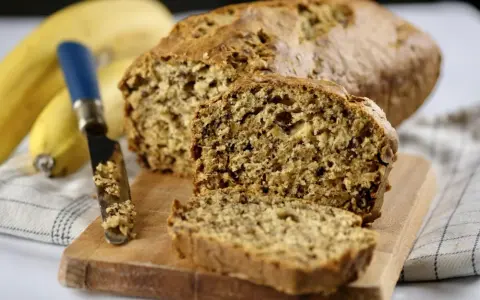 Pyszny chlebek bananowy, świeżo upieczony, z widocznym nożem i bananami w tle. Idealny na śniadanie.