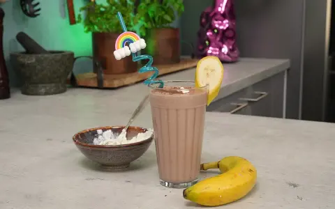 Ein leckerer schoko protein shake mit Banane und einem lustigen Regenbogen-Strohhalm. Daneben eine Schale mit Quark.