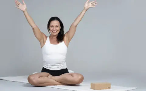 Kvinna i meditationsställning med armarna uppåt, utstrålar lugn och glädje. Hon praktiserar metta meditation för inre frid.
