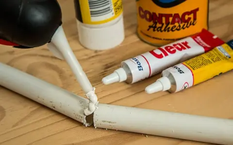 Klej w tubce i pistolet do klejenia na drewnianym blacie. Zastanawiasz się, czym usunąć klej super glue z mebli?