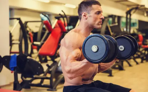 Hombre concentrado realizando ejercicios de bíceps con mancuernas en el gimnasio.