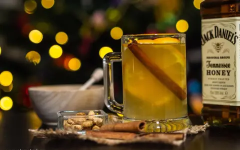 Rozgrzewający drink z Jack Daniels Tennessee Honey, z pomarańczą i cynamonem, w blasku świątecznych światełek.