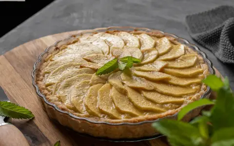 Tarta de manzana casera, con láminas de manzana doradas y una hoja de menta fresca en el centro.