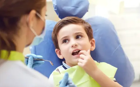Chłopiec u dentysty, martwiący się o zbyt wczesne wypadanie zębów mlecznych.