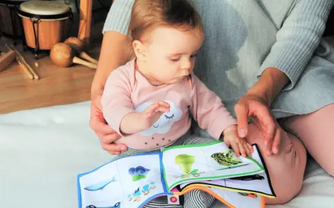 Baby lernt mit einem Stoffbuch und Musikinstrumenten. Förderung der sprachentwicklung baby.