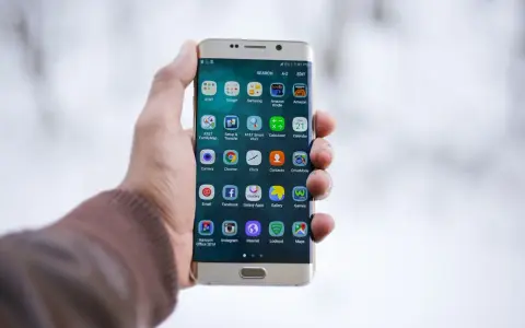Dłoń trzymająca złoty telefon Samsung z ikonami aplikacji na ekranie.