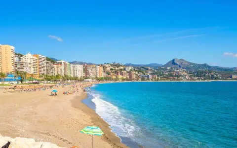 En solig dag på malaga strand med turkost vatten, sand och en stadskant i bakgrunden. En perfekt plats för avkoppling.