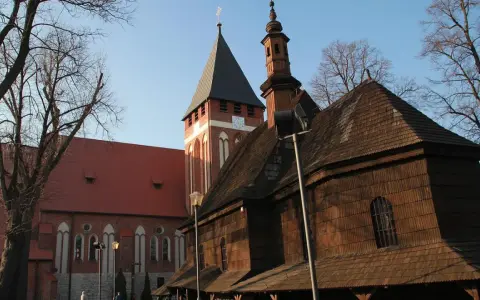 Drewniana i ceglana architektura kościołów w miasteczku śląskim, z wieżą zegarową i strzelistymi dachami, pod błękitnym niebem.