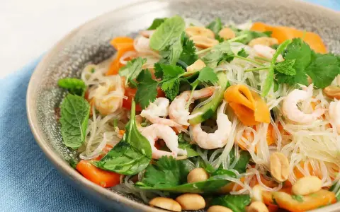 En läcker asiatisk nudelsallad med räkor, morötter, gurka, jordnötter och färska örter.