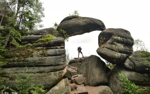 Turysta stoi na skale pod skalnym łukiem w Broumovskich Ścianach.