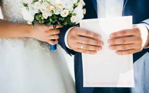 Para weselna trzyma bukiet i dokument. Na palcach widać obrączki. Co się daje na wesele? Dokumenty i kwiaty to symboliczne dary.
