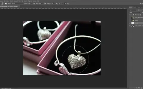 Un collier en forme de cœur orné de strass, dans une boîte rose. Un effet lumière Photoshop est appliqué pour le faire scintiller.