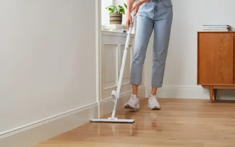 Person wischt den Holzboden, um die Wohnung zu reinigen. Ein moderner Wischmopp gleitet über das glänzende Parkett.