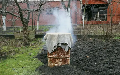Dym unosi się z beczki, która służy jako prowizoryczna wędzarnia. Wokół niej widać ziemię i trawę.