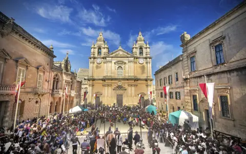 Tłum ludzi w historycznych strojach zgromadzony na placu przed katedrą w Mdina, Malta.