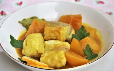Sabroso cazon en amarillo, con trozos de pescado blanco y patatas en una salsa dorada, decorado con perejil y rodajas de limón.