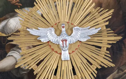 Ein silberner Taube mit ausgebreiteten Flügeln vor einem goldenen Strahlenkranz. Dies symbolisiert den Heiligen Geist und was bedeutet Pfingsten: die Ausgießung des Geistes.