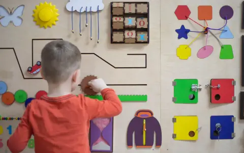 Chłopiec bawi się na tablicy edukacyjnej, rozwijając zdolności manualne. To świetna metoda montessori dla małych odkrywców.