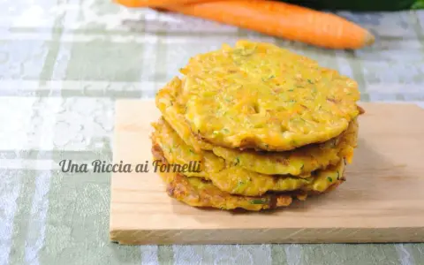 Pancakes dorati di frittata con farina di ceci, serviti su un tagliere di legno, con carote sullo sfondo.