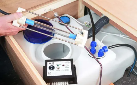 Ein Gerät zur UV-Wasserdesinfektion hilft, das Wasser frisch zu halten. Eine Hand hält eine UV-Lampe über einem Wassertank.