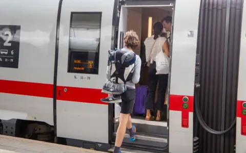 Reisende steigen in den ICE ein, um die ICE strecken zu befahren. Ein junger Mann mit Rucksack und Schuhen am Gepäck steigt als Erster ein.
